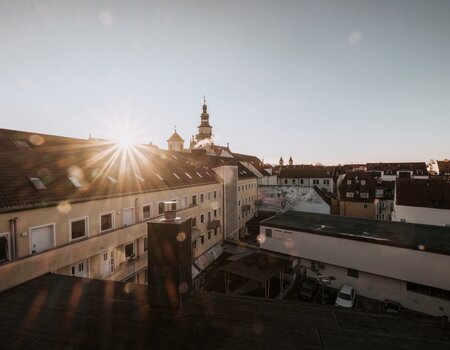 Sonnenuntergang über den Dächern der Stadt mit historischem Kirchturm.